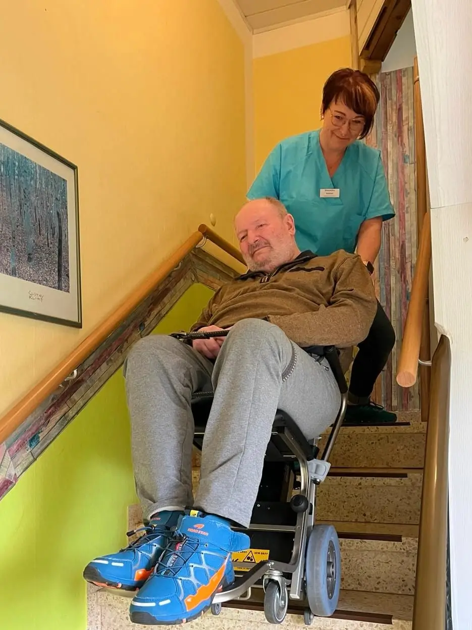 Eine Pflegekraft begleitet einen Klienten im Treppensteiger sicher die Treppe hinunter