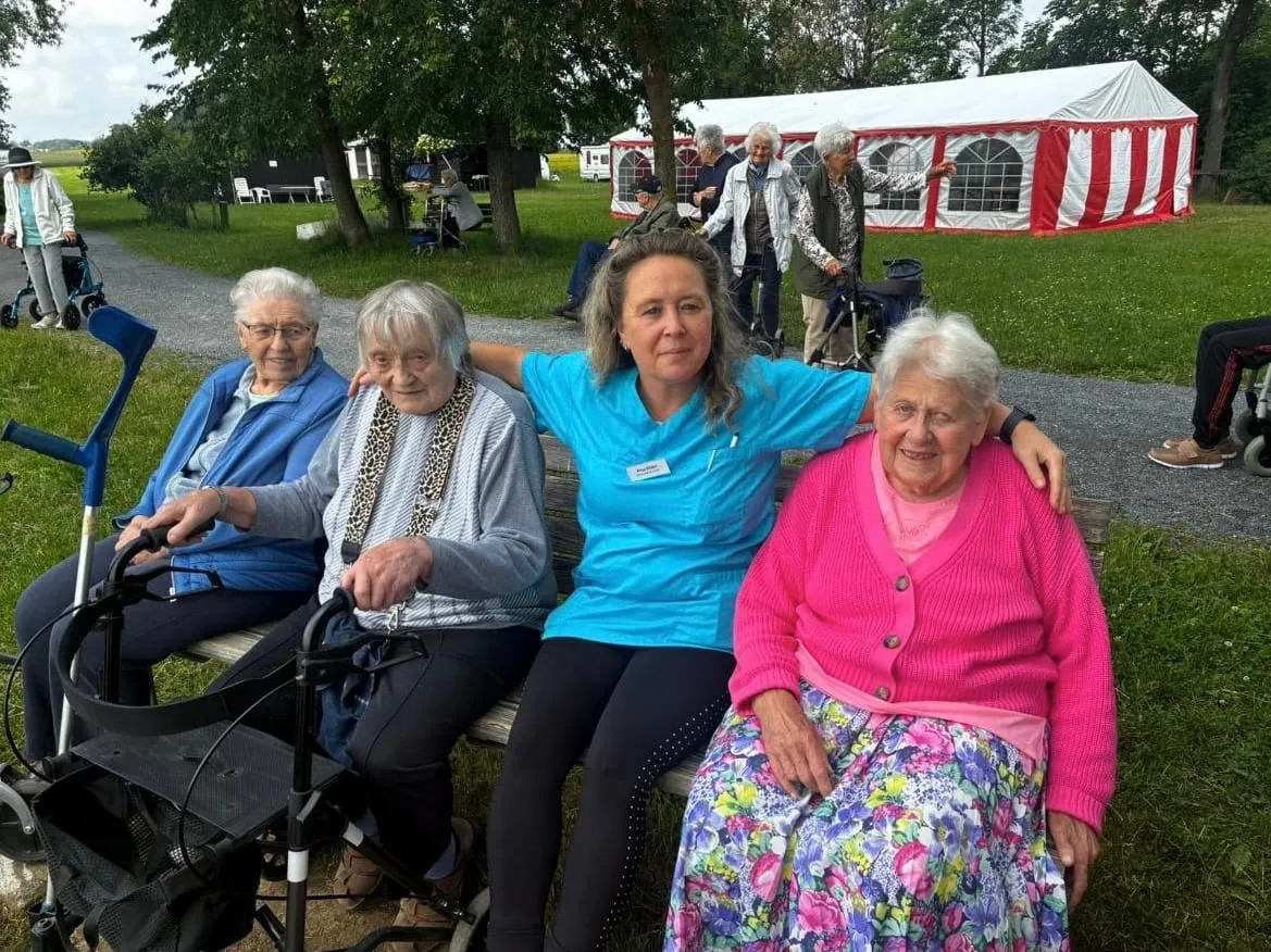 Eine Betreuerin sitzt beim Sommerfest mit drei Gästinnen auf einer Bank im Freien