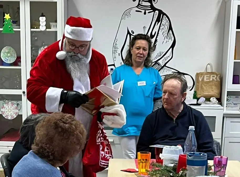 Der Nikolaus besucht die Gäste am Tisch, eine Betreuerin steht daneben