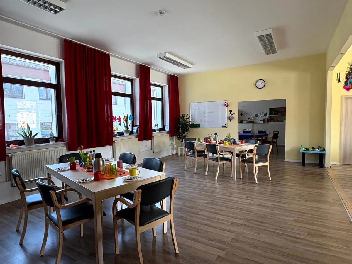 Großer Aufenthaltsraum mit gedeckten Tischen, roten Vorhängen und breiter Fensterfront