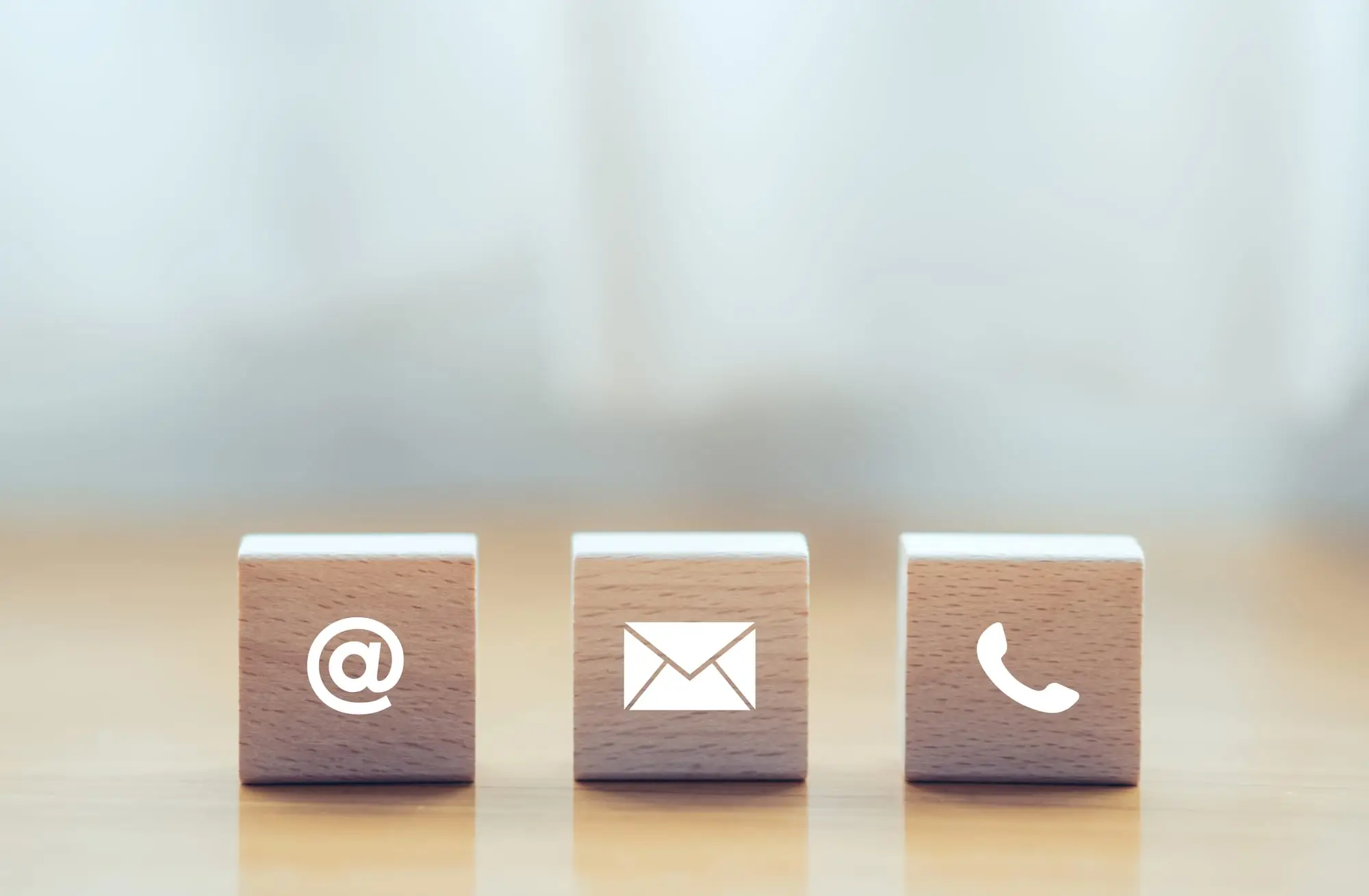 Drei Holzwürfel mit Symbolen für E-Mail, Brief und Telefonhörer