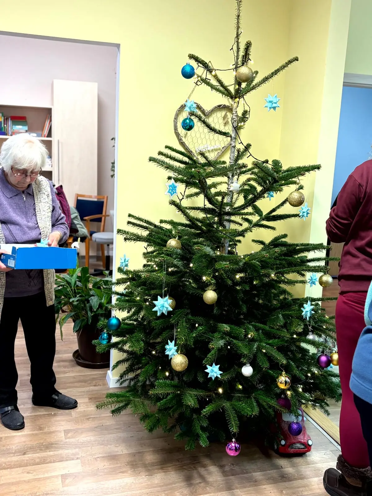 Eine Gästin steht mit einem kleinen Geschenk neben dem geschmückten Weihnachtsbaum